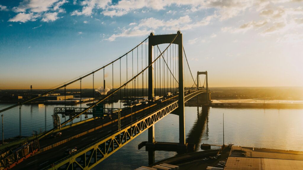 pexels-photo-6572480-6572480 Breathtaking metal long bridge with cars over calm river under bright blue cloudy sky